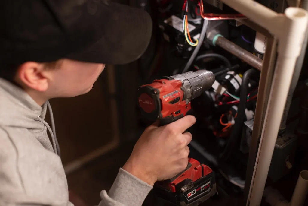 HVAC Comfort tech drills into heating unit.