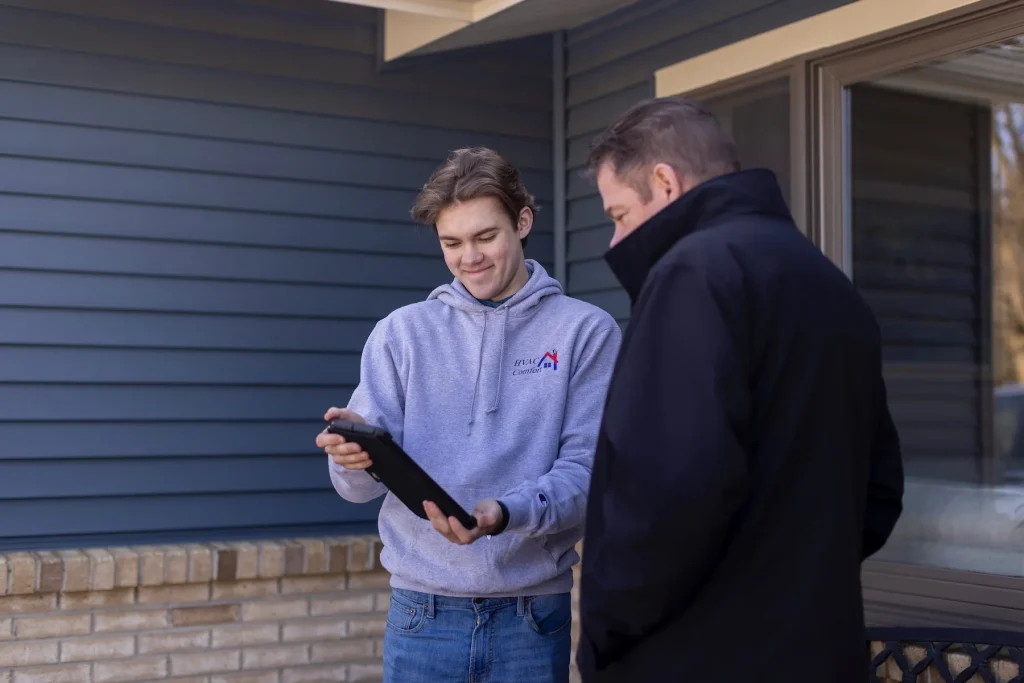 An HVAC Comfort tech talking with a customer outside of their house going over FAQs.